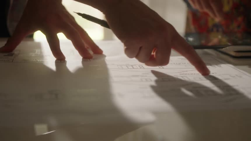 The view is of two people that are indoors pointing at house plans