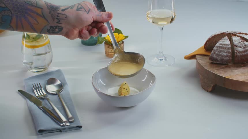 Someone serving some kind of yellow soup with an elegant table
