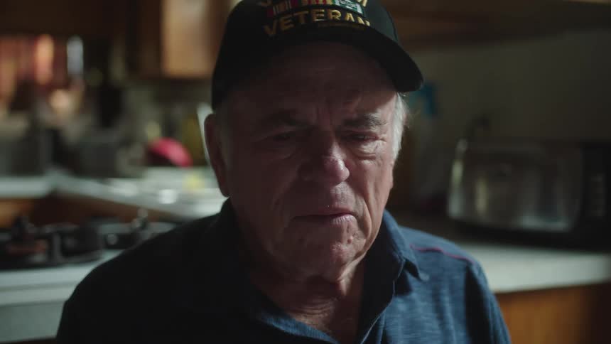 Elderly man sits sighing and frowning near kitchen