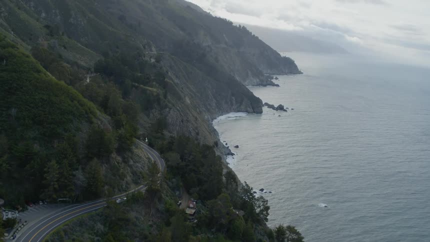 Highway winds along mountain overlooking misty coast on cloudy day