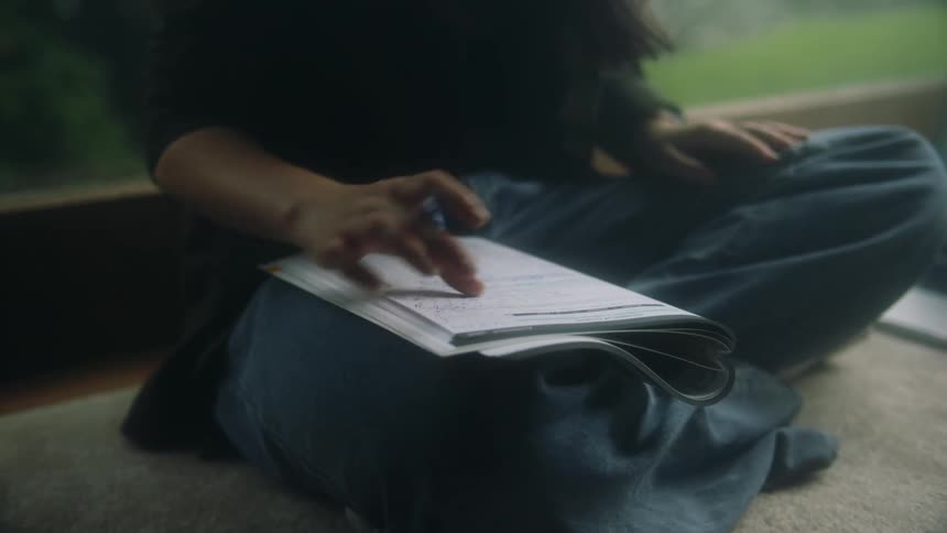 Woman sits on floor near window completing homework