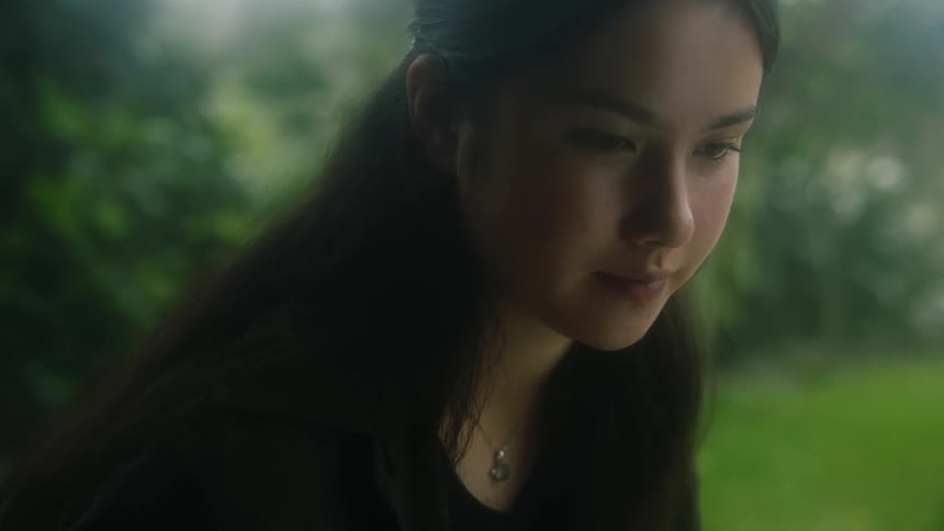 Woman sitting on lawn looks up from task and thinks with a small smile