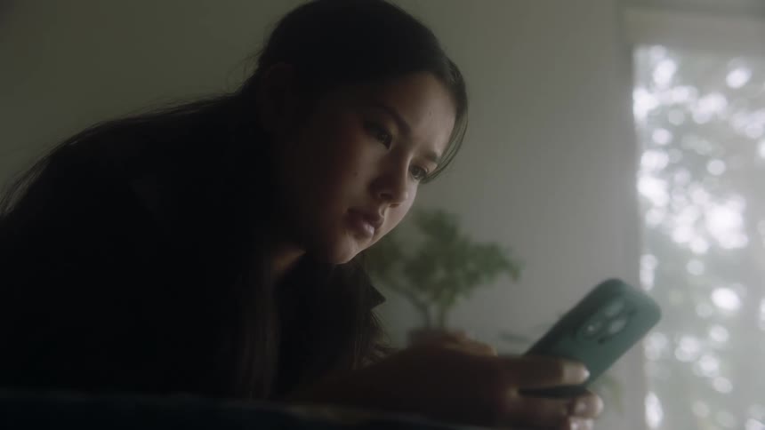 Woman sitting in dimly lit room scrolls on her smartphone