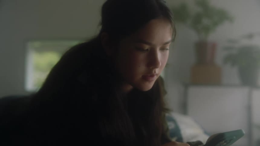A teenage girl sits with her smartphone in her hand scrolling and talking to herself