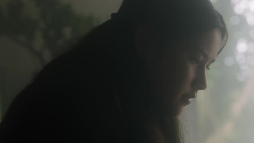 Woman in dim room near plant concentrates on task