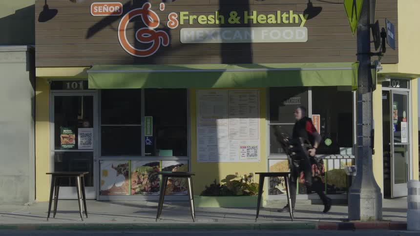 Restaurant worker places chairs on sidewalk near busy street