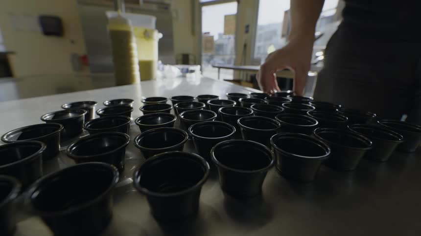 Restaurant worker lines small sauce cups on counter as traffic passes on street in the background