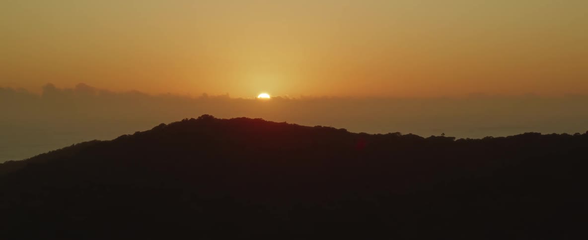 An aerial view of a sunrise over a mountain and the ocean