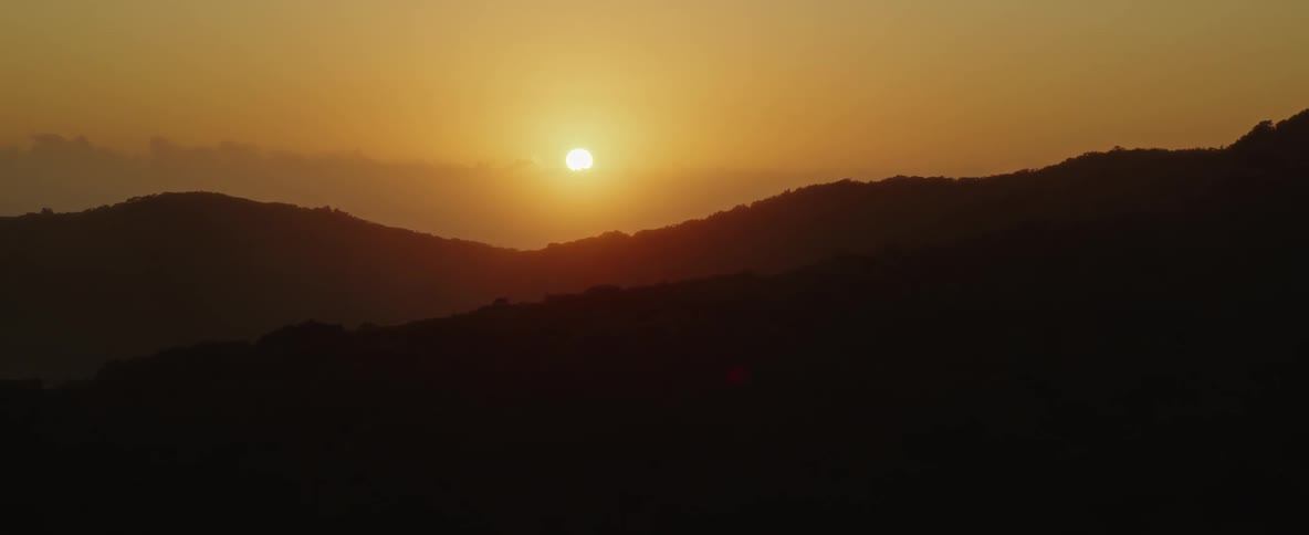 A glowing sun in a golden sky above mountain ridges