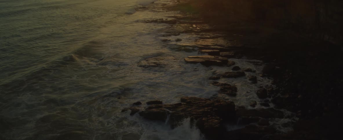Waves crashing against rocks on the coast as the sun setting reflects off the water and rocks