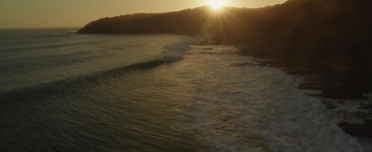 Waves roll in to shore and over the beach as the sun sets over the promontory