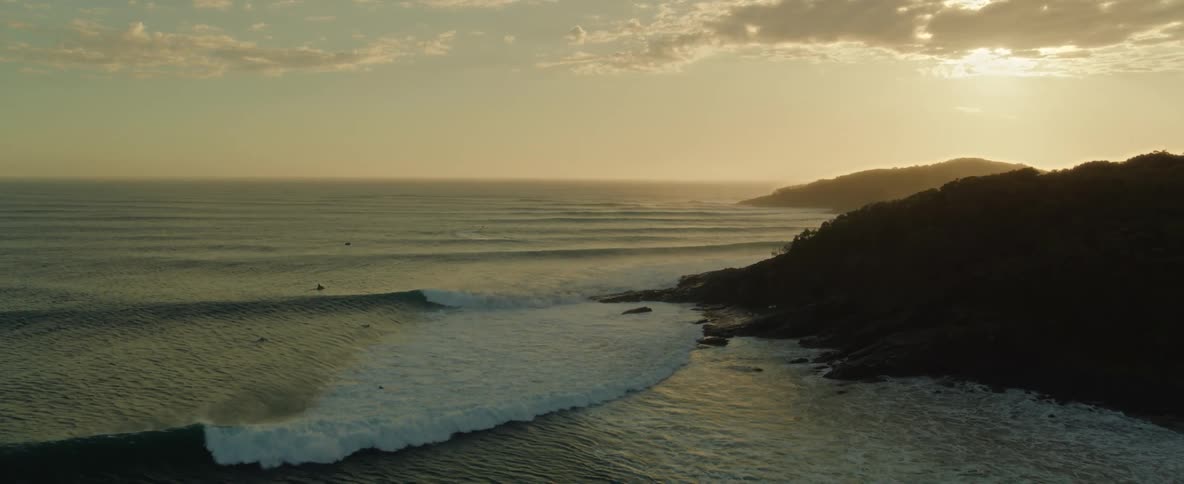 Aerial view of ocean waves breaking against the coastline at sunset