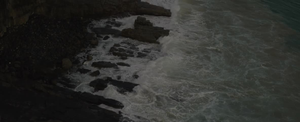 An aerial of waves from the ocean crashing against the rocky coast