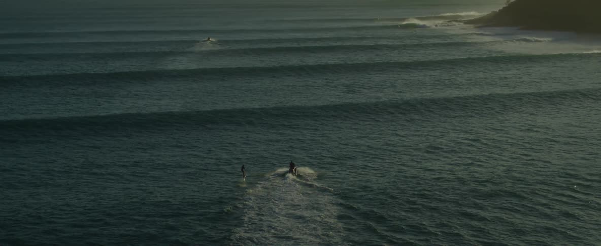A person rides a jet ski while pulling a water skier across ripples of ocean waves