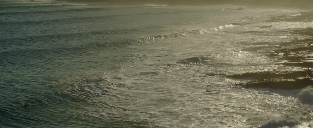 Surfers are standing on a large rock and diving into the ocean waves