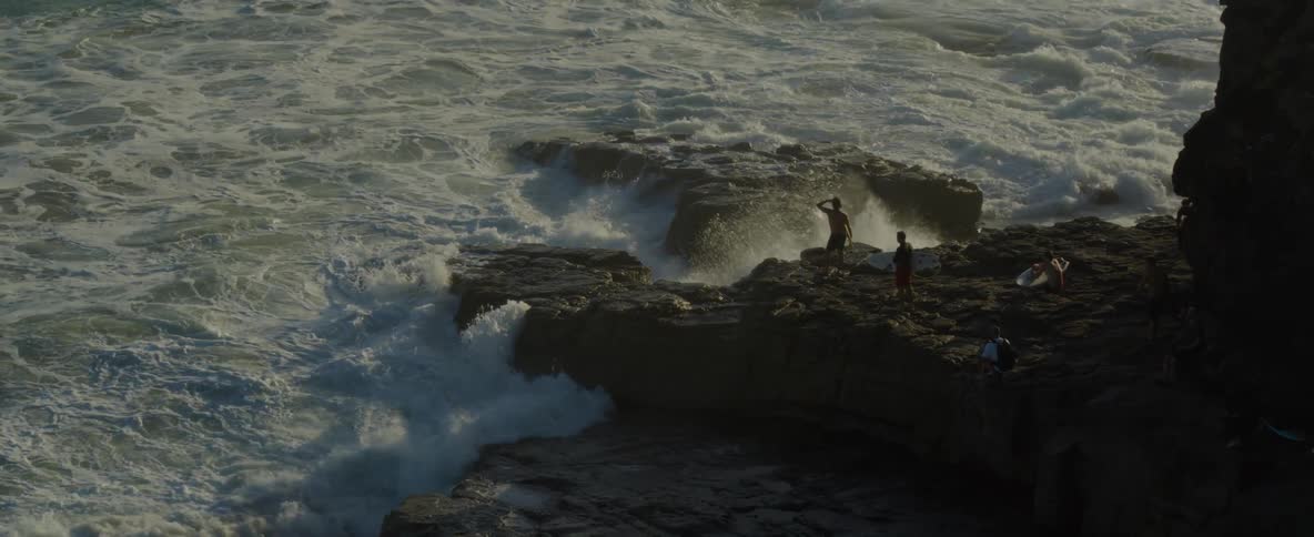 Aerial view of a group of young people with surfboards standing over the rocks next to the ocean