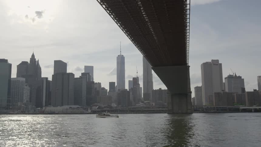 A boat going under a bridge that spans across a body of water to a city