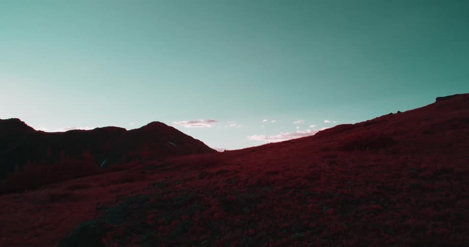 Colored filter tints vegetation on mountainside red under green tinted sky