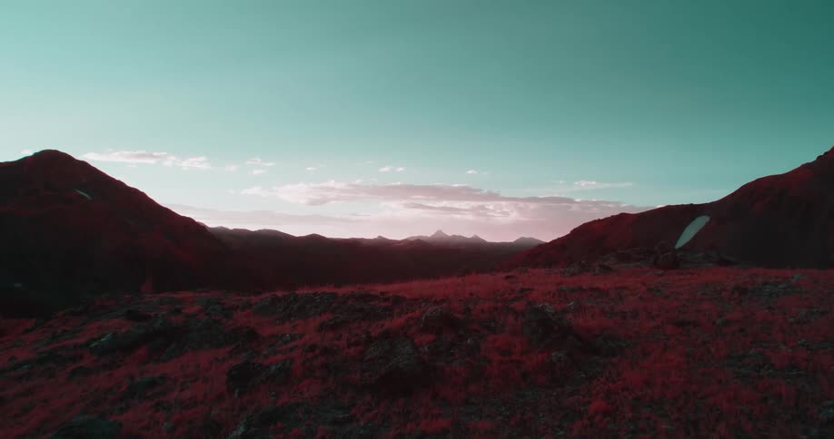 A hill is shown with red grass and brown dirt and there are mountains in the background