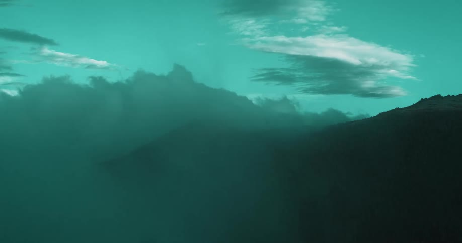 Low lying clouds flow over the red tinted silhouette of a mountain