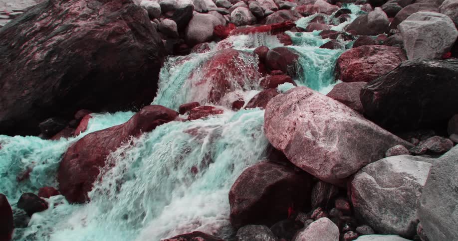 Green tinted white water flows over red tinted boulders