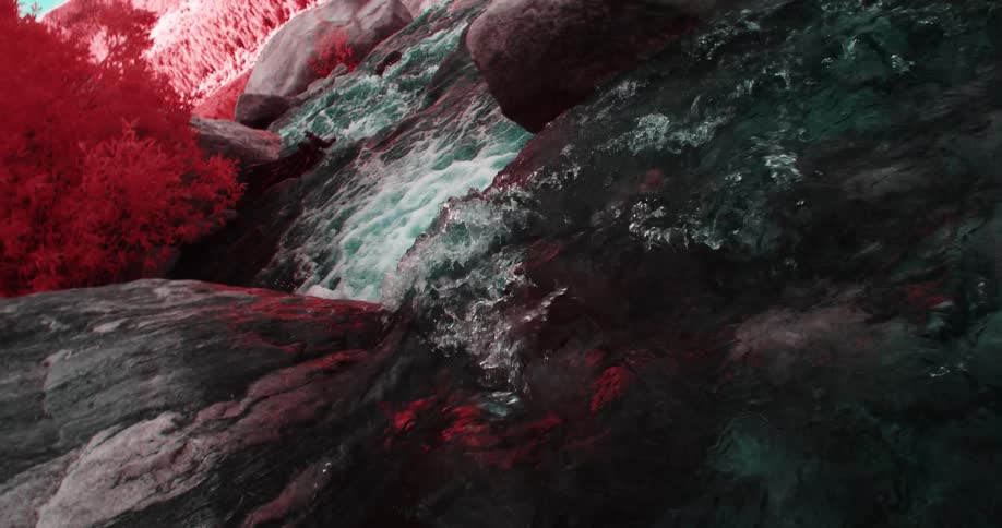 Water flows over rocks and between boulders toward red tinted landscape