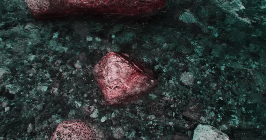 Water flows past red tinted rocks and over smaller stones