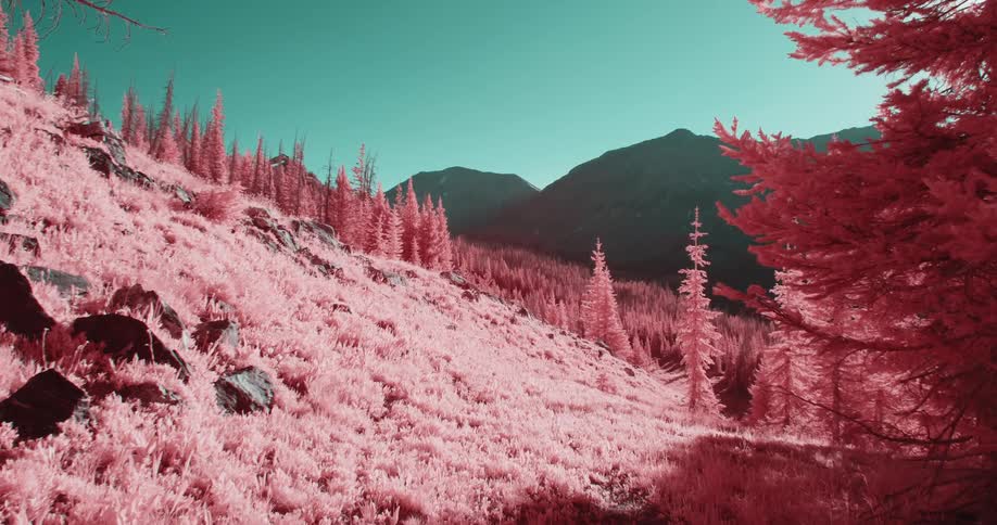 Sun glares onto red tinted land contrasting with silhouetted mountains under aquamarine blue sky