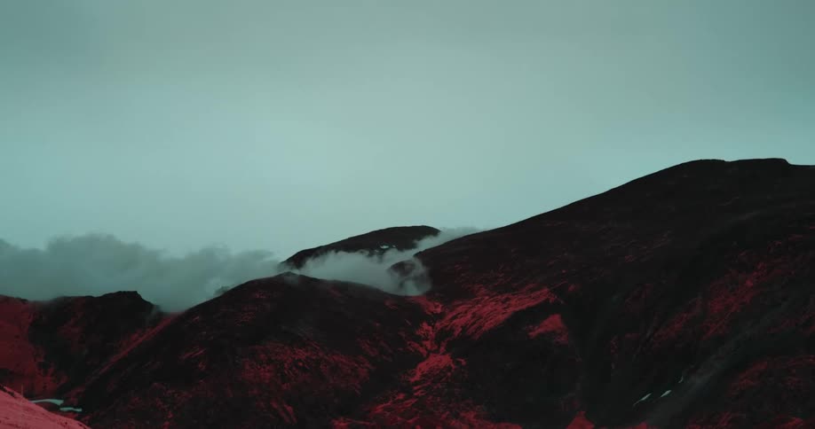 Low lying clouds flow over red tinted hills and mountains