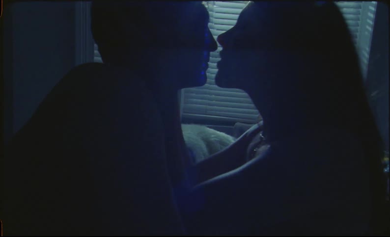 Light shining brightly through blinds at night illuminates silhouettes of man and woman kissing in bedroom