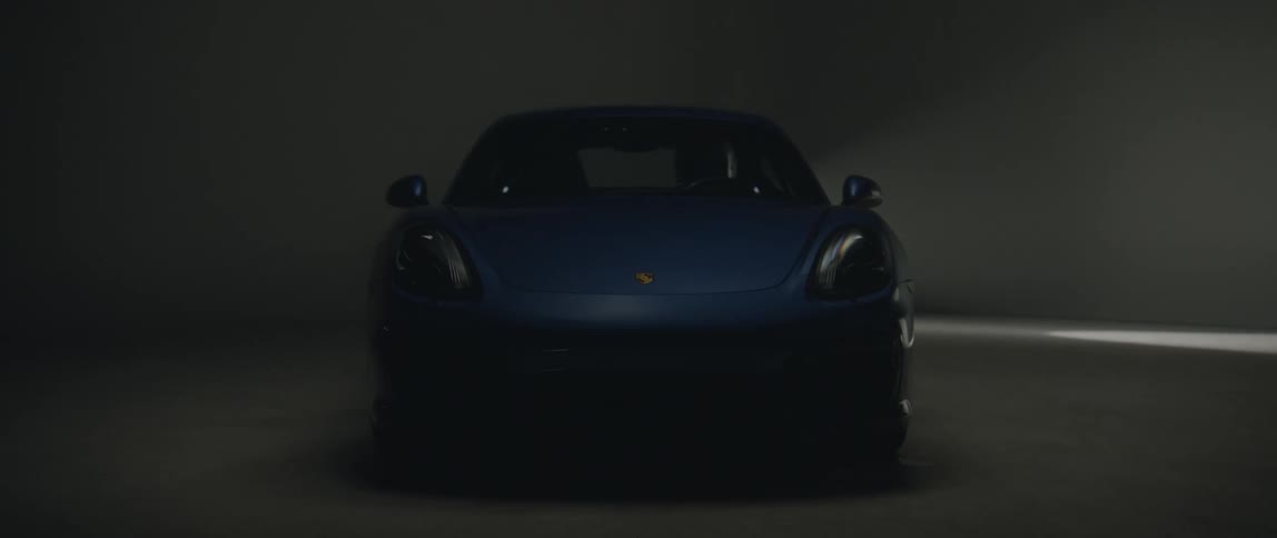 Spotlight sweeps back forth over blue sports car parked in dimly lit area