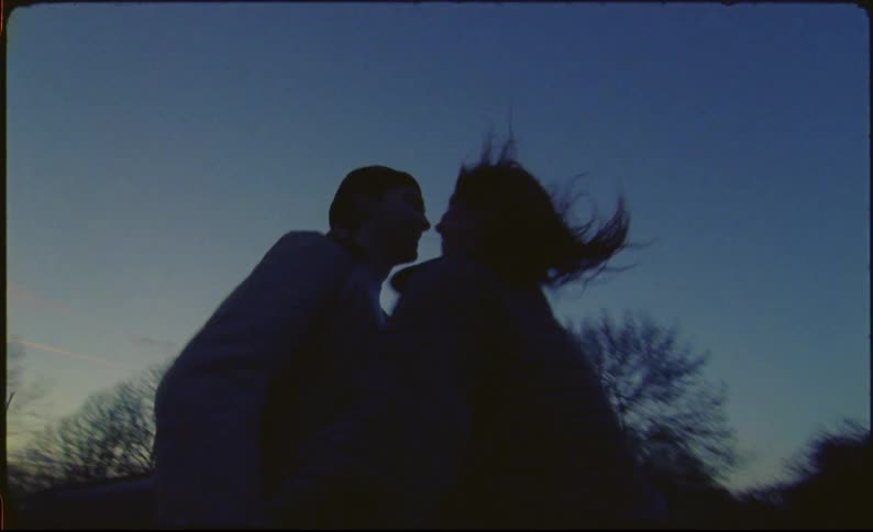 Couple runs hand in hand along sidewalk at night before stopping to kiss