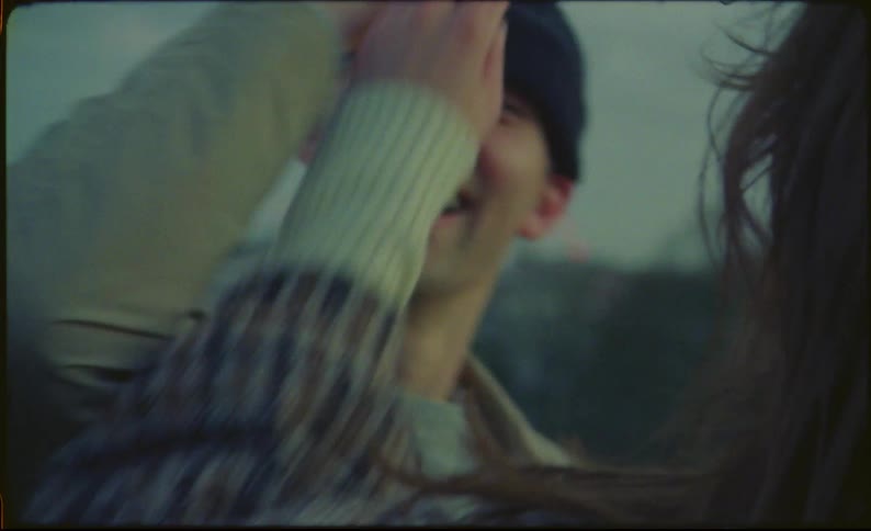 Woman teases man by pulling his knit hat over his face as they stand outdoors