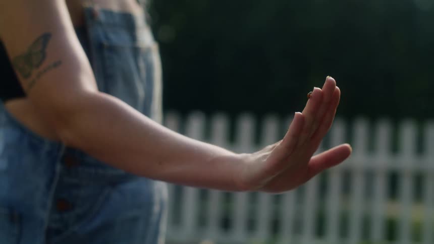 A woman is standing outside with a ladybug on her hand that is crawling all over her fingers