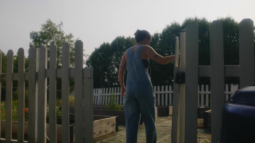 Woman opens gate and walks into area with multiple raised gardening beds