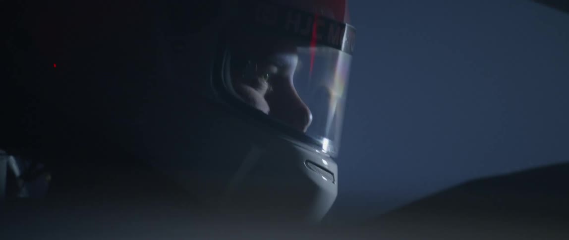 Racecar driver wearing crash helmet steers car past hills at night