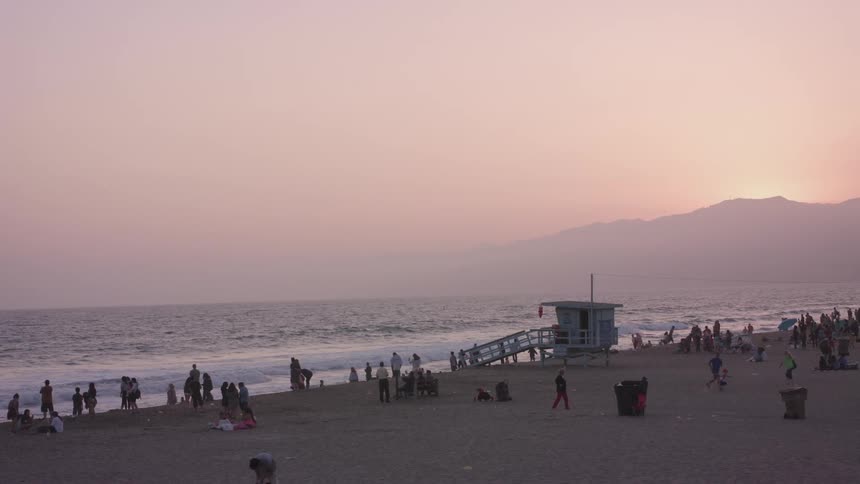 People play and stand on a beach at dusk