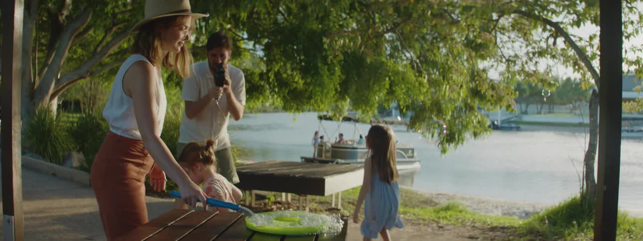 A father video recording his daughters play in bubbles the mother is lifting out of the tray