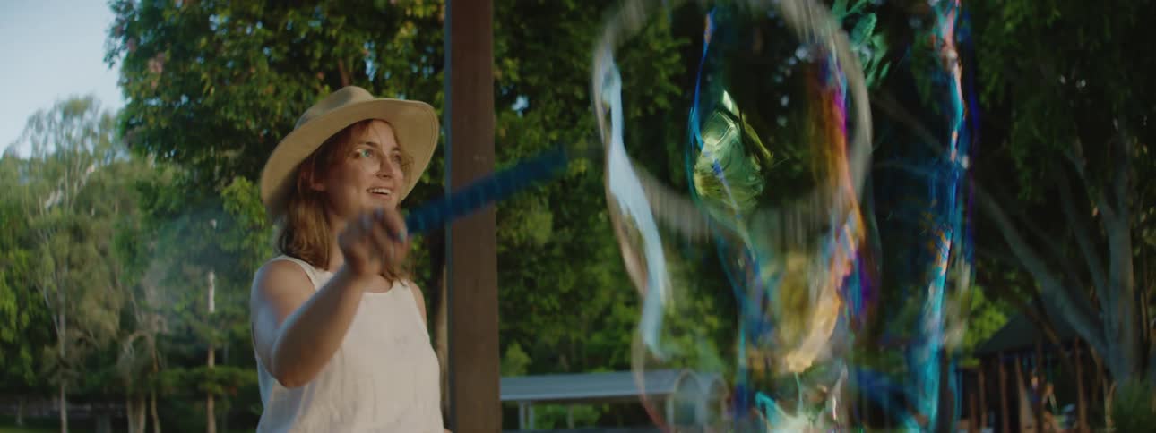 A woman smiles as she creates enormous bubbles while outdoors