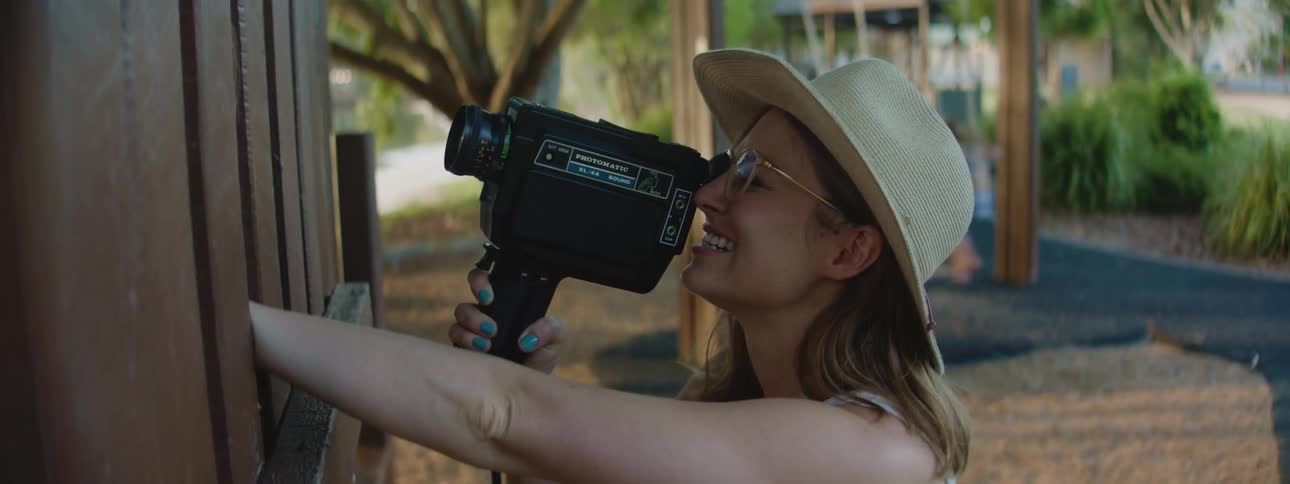 A close up of a mother holding a video camera recording someone in front of her on a play set