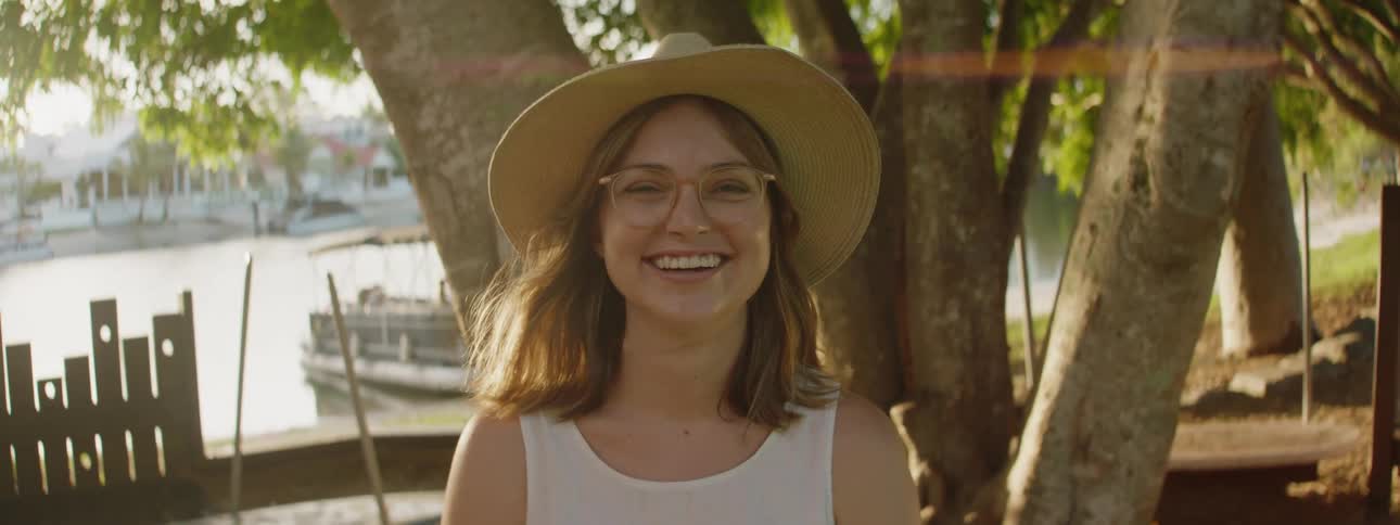 A young lady wearing a hat and glasses joyfully laughing while looking at the camera