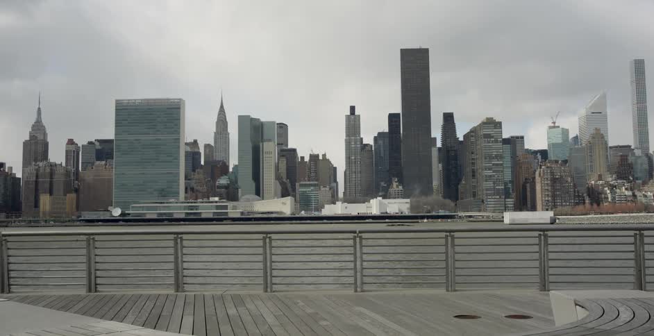 A large city sits beyond a boardwalk and a bay