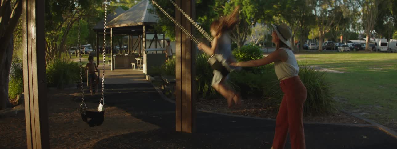 Mother is pushing her daughter on the swing set outdoors
