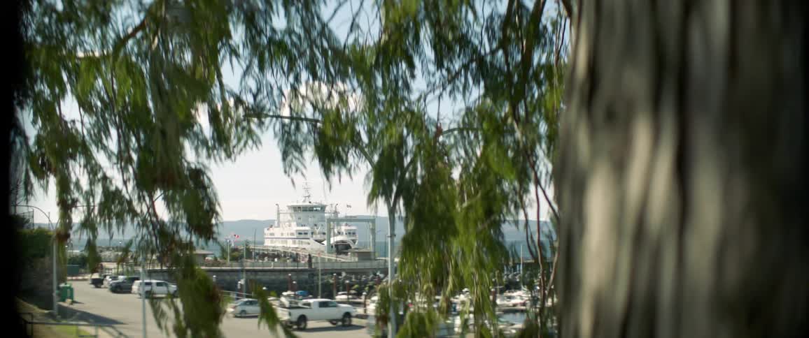 Several vehicles are parked in a lot nearby a dock leading to an idle boat