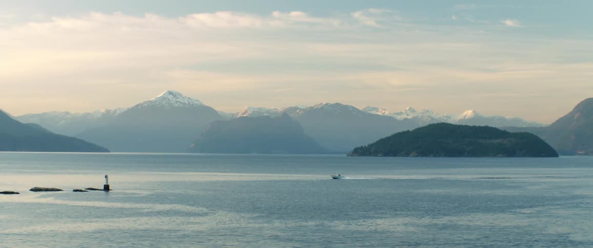 A boat speeds through the ocean in front of snow topped mountains