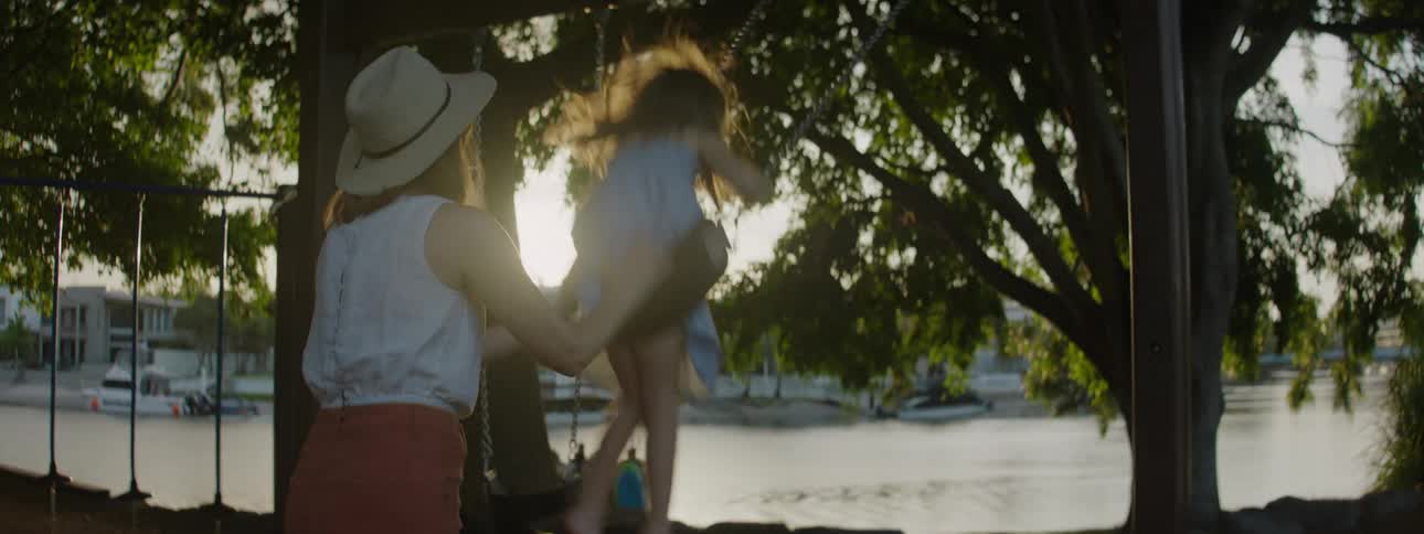 A mother is pushing her daughter on the swing