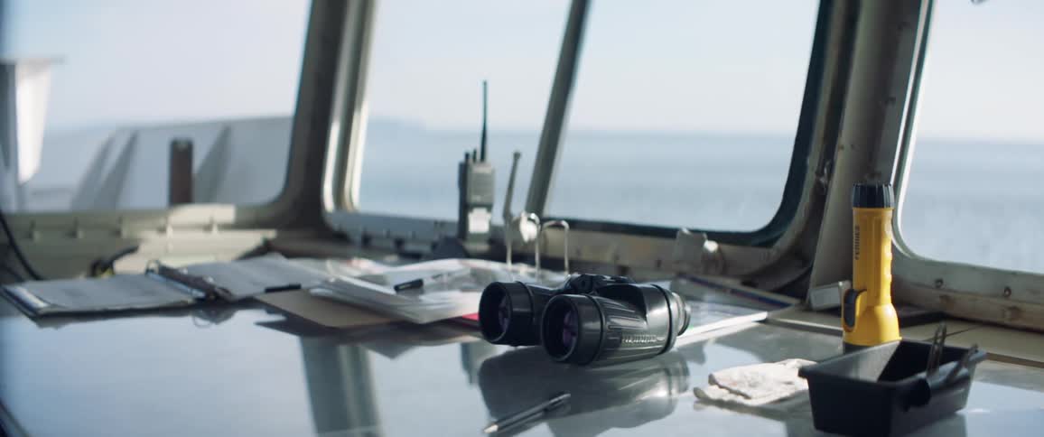 A table on a boat in the ocean is covered with papers binoculars a walkie talkie and other knick knacks