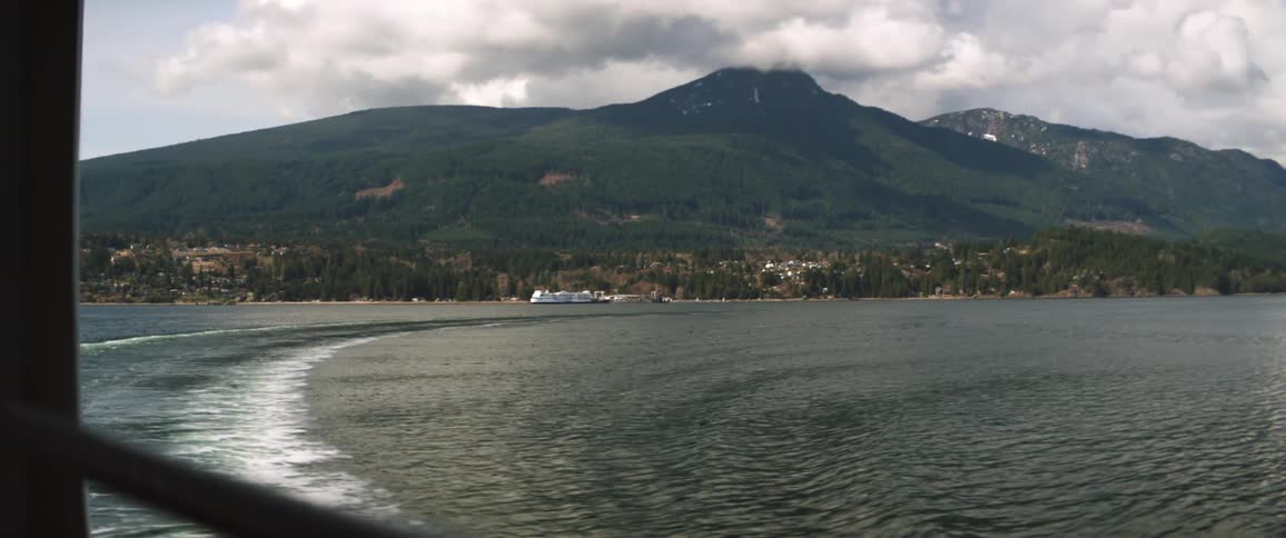A mountain covered in greenery looming over a coastal town seen from the deck of a ship