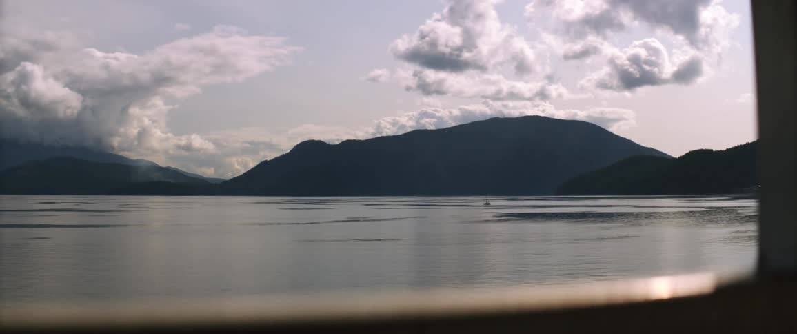 Clouds looming of a large surrounded by tall hills during the day