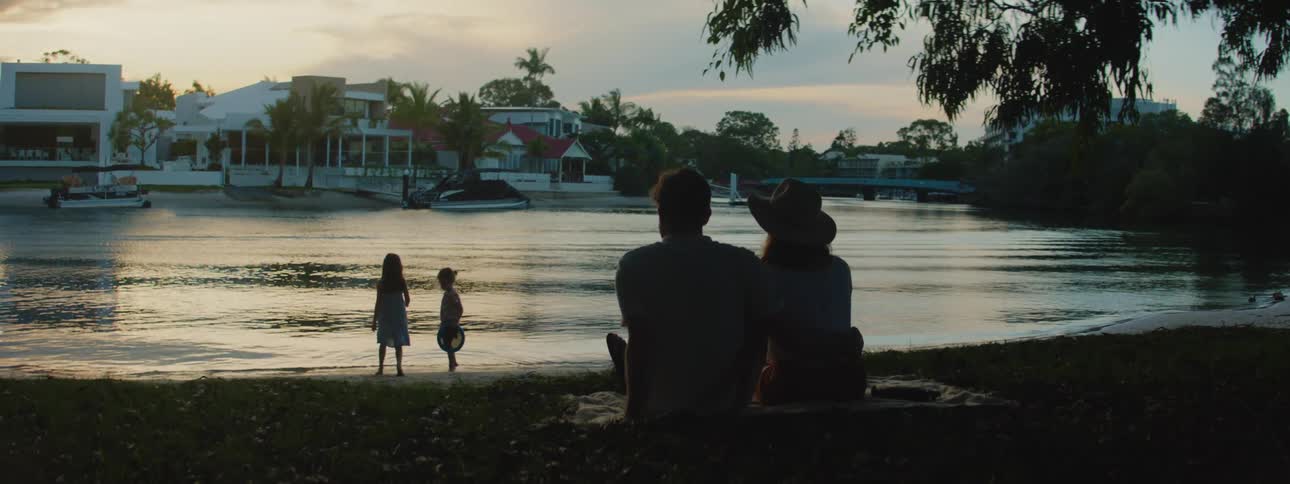 A couple watches their two girls play by the lake at dusk